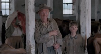 Movie still from “Pelle the Conqueror” (1987), directed by Bille August – A man standing next to a young boy in a barn; Medium shot, Low angle