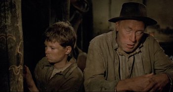 Movie still from “Pelle the Conqueror” (1987), directed by Bille August – A man sitting next to a young boy in a hat; Close Up shot, Low angle