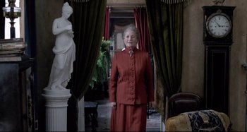 Movie still from “Pelle the Conqueror” (1987), directed by Bille August – An older woman in a red suit standing in a room; Medium shot, Low angle