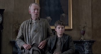 Movie still from “Pelle the Conqueror” (1987), directed by Bille August – A man and a young boy sitting next to each other; Medium shot, Low angle