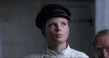 Movie still from “Pelle the Conqueror” (1987), directed by Bille August – A young boy wearing a hat looking up at the sky; Close Up shot, Low angle