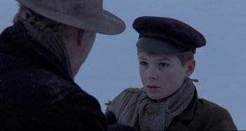 Movie still from “Pelle the Conqueror” (1987), directed by Bille August – A young boy wearing a hat and a scarf is talking to an older man; Close Up shot, Over the shoulder angle
