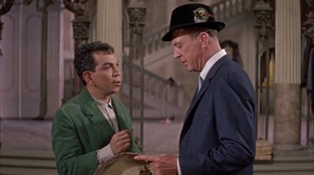 Movie still from “Pepe” (1960), directed by George Sidney – A man in a suit and hat talking to another man in a green suit; Medium shot, Over the shoulder angle