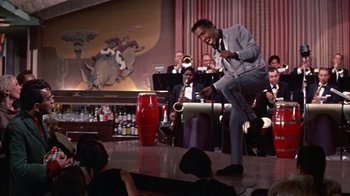 Movie still from “Pepe” (1960), directed by George Sidney – A man standing on a stage holding a saxophone; Wide shot, Low angle