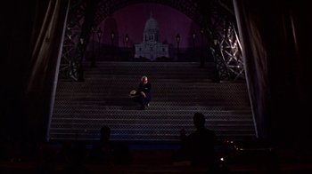 Movie still from “Pepe” (1960), directed by George Sidney – A man sitting on a staircase in front of a building; Extreme Wide shot, High angle