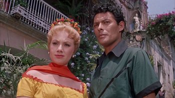 Movie still from “Pepe” (1960), directed by George Sidney – A man and a woman standing next to each other in front of flowers; Medium shot, Low angle