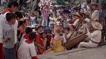 Movie still from “Pepe” (1960), directed by George Sidney – A group of people gathered around a woman in a yellow dress; Wide shot, High angle
