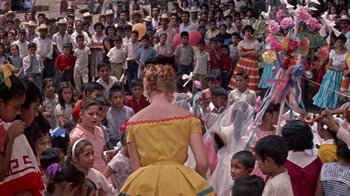Movie still from “Pepe” (1960), directed by George Sidney – A crowd of people gathered around a woman in a yellow dress; Medium shot, High angle