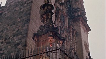Movie still from “Pepe” (1960), directed by George Sidney – A man standing on a balcony next to a tall building; Wide shot, Low angle