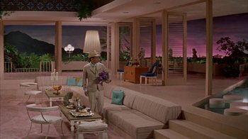 Movie still from “Pepe” (1960), directed by George Sidney – A man holding a bouquet of flowers standing in front of a living room; Wide shot, High angle