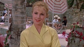 Movie still from “Pepe” (1960), directed by George Sidney – A woman in a yellow shirt standing under an umbrella in front of palm trees; Close Up shot, Low angle