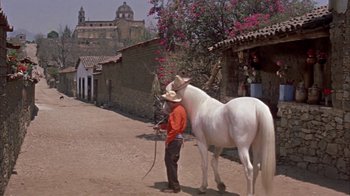 Movie still from “Pepe” (1960), directed by George Sidney – A man standing next to a white horse on a dirt road; Wide shot, Low angle