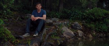 Movie still from “Percy Jackson: Sea of Monsters” (2013), directed by Thor Freudenthal – A man sitting on a rock near a body of water; Wide shot, High angle
