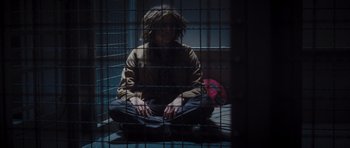 Movie still from “Percy Jackson: Sea of Monsters” (2013), directed by Thor Freudenthal – A person sitting on the ground inside a cage; Wide shot, Low angle