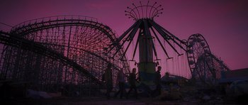 People walking in front of a roller coaster at dusk