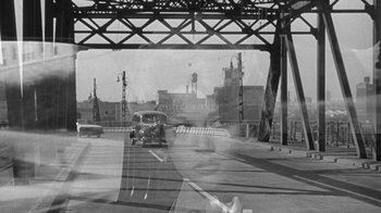 Movie still from “Period of Adjustment” (1962), directed by George Roy Hill – A black and white photo of a car driving down a street; Close Up shot, High angle