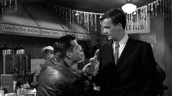Movie still from “Period of Adjustment” (1962), directed by George Roy Hill – A man talking to another man holding a bottle; Medium shot, Low angle
