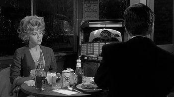 Movie still from “Period of Adjustment” (1962), directed by George Roy Hill – A man and a woman sitting at a dinner table in front of an old jukebox; Medium shot, Over the shoulder angle