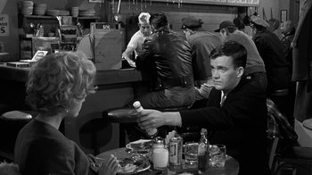 Movie still from “Period of Adjustment” (1962), directed by George Roy Hill – A man sitting at a table in front of two other people; Medium shot, Over the shoulder angle