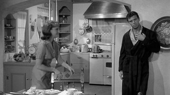 Movie still from “Period of Adjustment” (1962), directed by George Roy Hill – A woman and a man standing in a kitchen; Medium shot, Over the shoulder angle