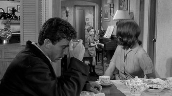 Movie still from “Period of Adjustment” (1962), directed by George Roy Hill – A man and a woman sitting at a table with a child in the background; Medium shot, Over the shoulder angle
