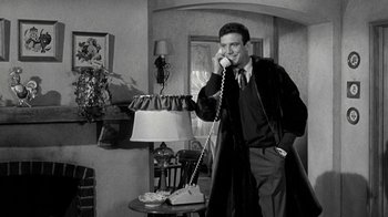 Movie still from “Period of Adjustment” (1962), directed by George Roy Hill – A man talking on a phone while standing next to a lamp; Medium shot, Low angle