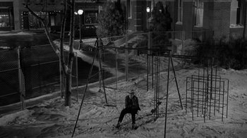 Movie still from “Period of Adjustment” (1962), directed by George Roy Hill – A person sitting in the snow on a swing set; Wide shot, High angle