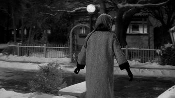 Movie still from “Period of Adjustment” (1962), directed by George Roy Hill – A person in a long coat walking in the snow near a lamp post; Medium shot, Low angle
