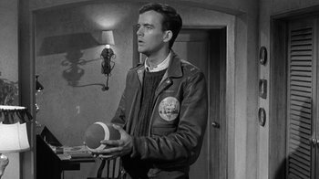 Movie still from “Period of Adjustment” (1962), directed by George Roy Hill – A black and white photo of a man holding a football; Medium shot, Over the shoulder angle