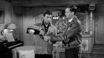 Movie still from “Period of Adjustment” (1962), directed by George Roy Hill – Two men in a room one is holding a wine bottle and the other is holding a beer; Medium shot, Over the shoulder angle