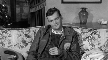 Movie still from “Period of Adjustment” (1962), directed by George Roy Hill – A black and white photo of a man sitting on a couch holding a drink; Medium shot, High angle