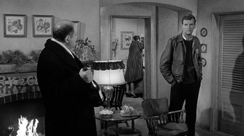 Movie still from “Period of Adjustment” (1962), directed by George Roy Hill – Two men standing in front of a lamp in a room; Medium shot, Over the shoulder angle