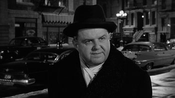 Movie still from “Period of Adjustment” (1962), directed by George Roy Hill – A man in a hat and a black coat standing in front of cars; Close Up shot, Over the shoulder angle