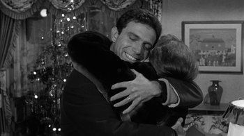 Movie still from “Period of Adjustment” (1962), directed by George Roy Hill – A man hugging another man in a room with lights in the background; Medium shot, Over the shoulder angle