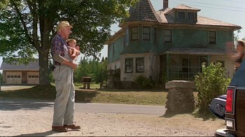 Movie still from “Pet Sematary” (1989), directed by Mary Lambert – An older man holding a baby in his arms; Wide shot, Low angle