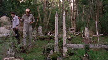 Movie still from “Pet Sematary” (1989), directed by Mary Lambert – An old man standing in front of a grave in the woods; Wide shot, High angle