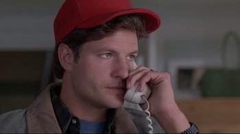 Movie still from “Pet Sematary” (1989), directed by Mary Lambert – A man wearing a red hat talking on a phone; Close Up shot, Low angle