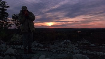 Movie still from “Pet Sematary” (1989), directed by Mary Lambert – A man standing on top of a rocky hill at sunset; Wide shot, Low angle