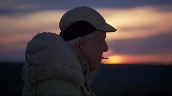 Movie still from “Pet Sematary” (1989), directed by Mary Lambert – An older man wearing a cap and jacket with a cigarette in his mouth at sunset; Close Up shot, Low angle
