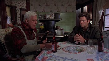 Movie still from “Pet Sematary” (1989), directed by Mary Lambert – Two men sitting at a table with a bottle of beer; Medium shot, High angle
