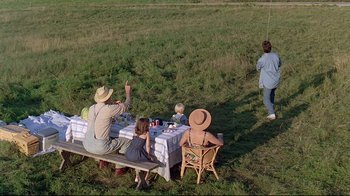 Movie still from “Pet Sematary” (1989), directed by Mary Lambert – A group of people sitting at a table in the grass; Wide shot, High angle
