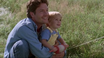 Movie still from “Pet Sematary” (1989), directed by Mary Lambert – A man and a child are sitting in a field; Medium shot, Low angle