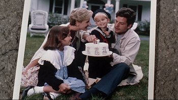 Movie still from “Pet Sematary” (1989), directed by Mary Lambert – A group of people sitting on the grass with a cake; Medium shot, High angle