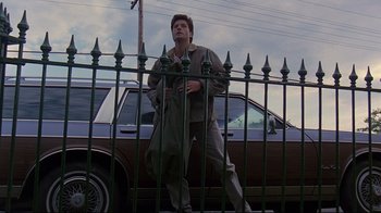 Movie still from “Pet Sematary” (1989), directed by Mary Lambert – A man standing next to a fence next to a car; Wide shot, Low angle