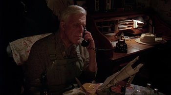 Movie still from “Pet Sematary” (1989), directed by Mary Lambert – An older man sitting at a table talking on the phone; Medium shot, High angle