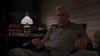 Movie still from “Pet Sematary” (1989), directed by Mary Lambert – An older man sitting in a chair in front of a lamp; Medium shot, Low angle