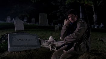 Movie still from “Pet Sematary” (1989), directed by Mary Lambert – A man sitting in the grass next to a grave at night; Medium shot, Low angle