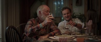 Movie still from “Pet Sematary” (2019), directed by Kevin Kölsch – Two men sitting at a dinner table drinking wine; Medium shot, Over the shoulder angle