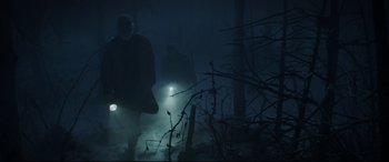 Movie still from “Pet Sematary” (2019), directed by Kevin Kölsch – Two people walking in the woods with lights on; Wide shot, Low angle