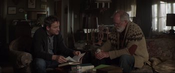 Movie still from “Pet Sematary” (2019), directed by Kevin Kölsch – Two men are sitting at a table with books and a can; Medium shot, Over the shoulder angle